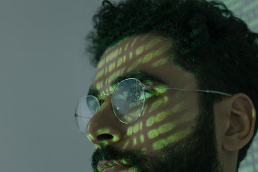 A man wearing glasses with binary code projected across his face, symbolizing cybersecurity.